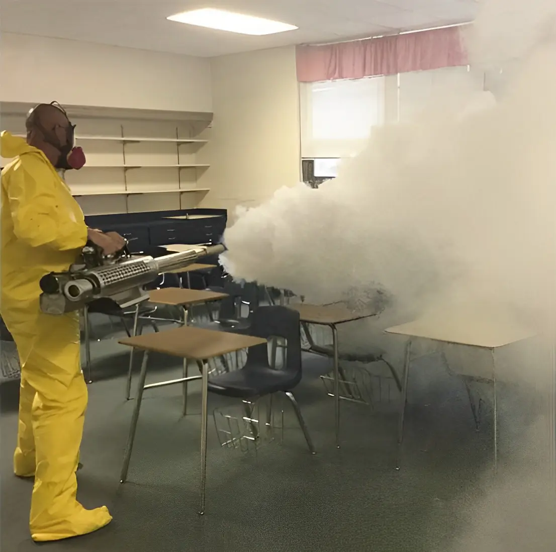 Person in yellow hazmat suit fumigating a classroom with a fogging machine.